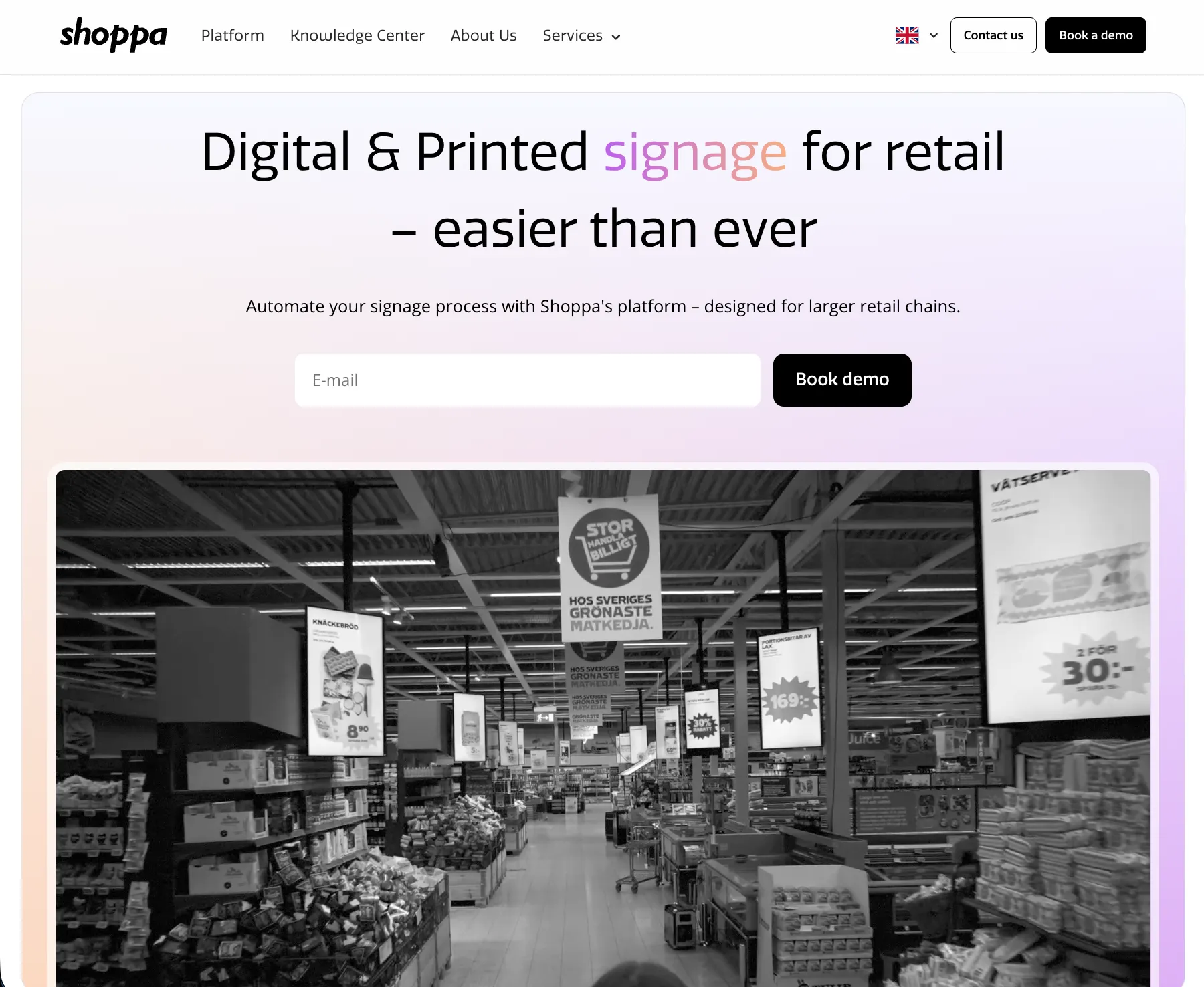 The rebuilt home page: the hero headline, a language switcher and a demo request form above a photograph of a supermarket aisle hung with printed and digital signage.